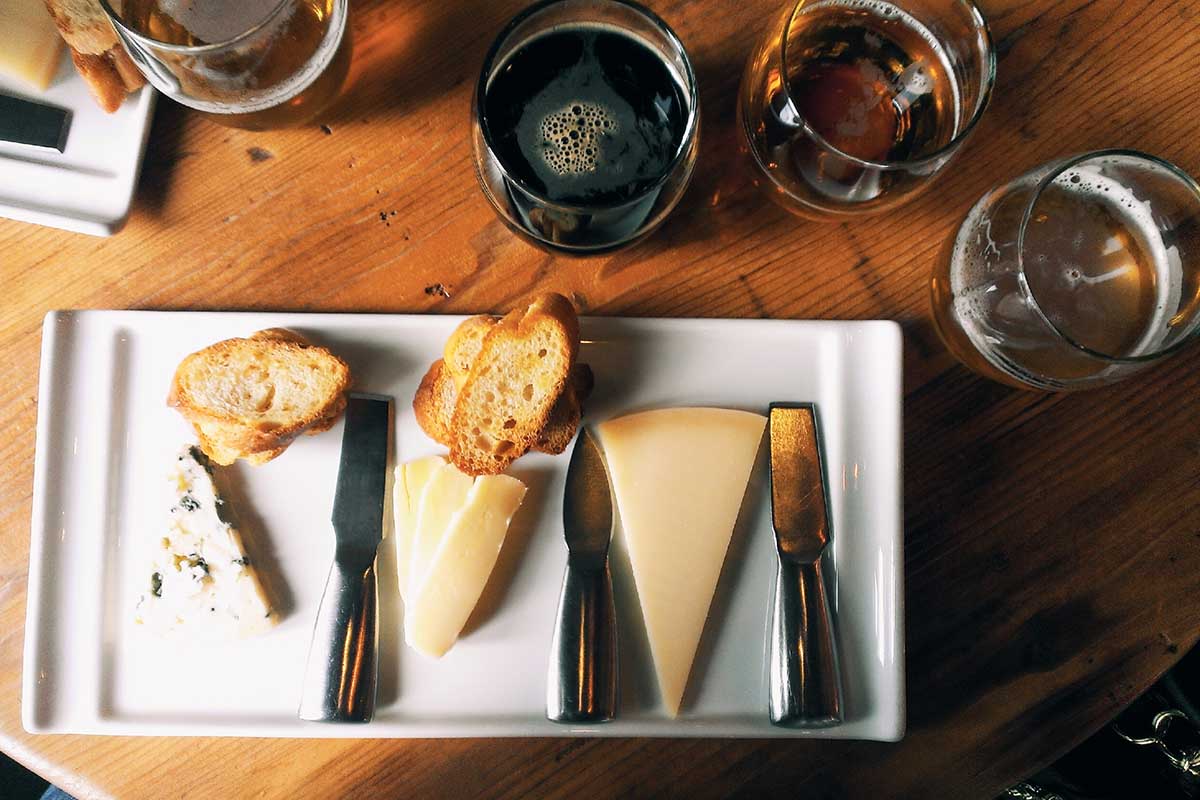 Directly Above Shot Of Cheese And Bread In Plate By Beer Glasses On Table. Beer and cheese can make for a better pairing than wine and cheese, according to some experts.