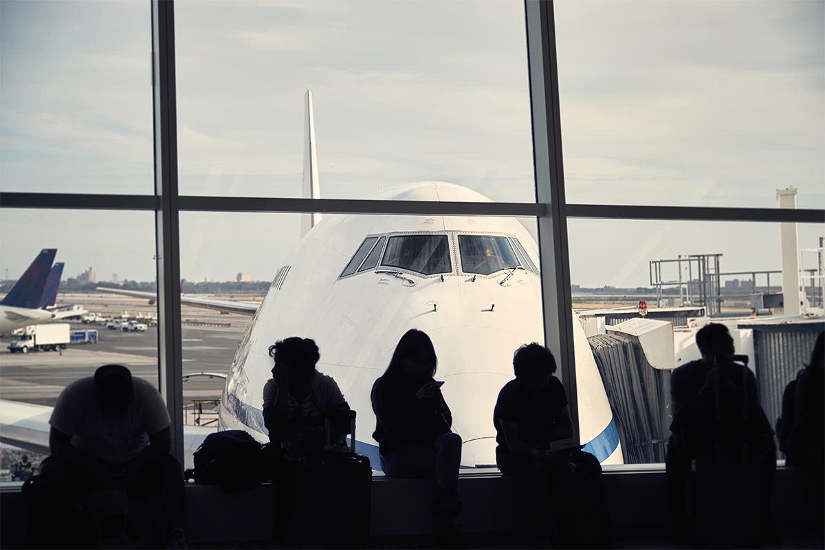 Passengers waiting in an airport terminal to board their outgoing commercial airplane flight.