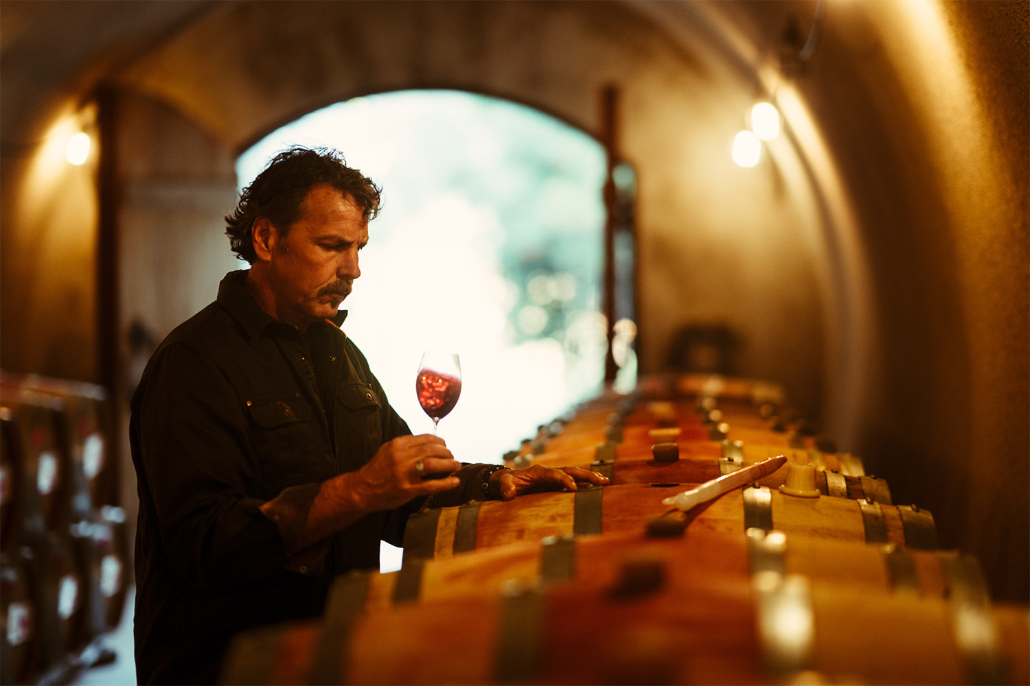 Napa Valley winemaker Chris Carpenter stands by barrels swirling a glass of red wine