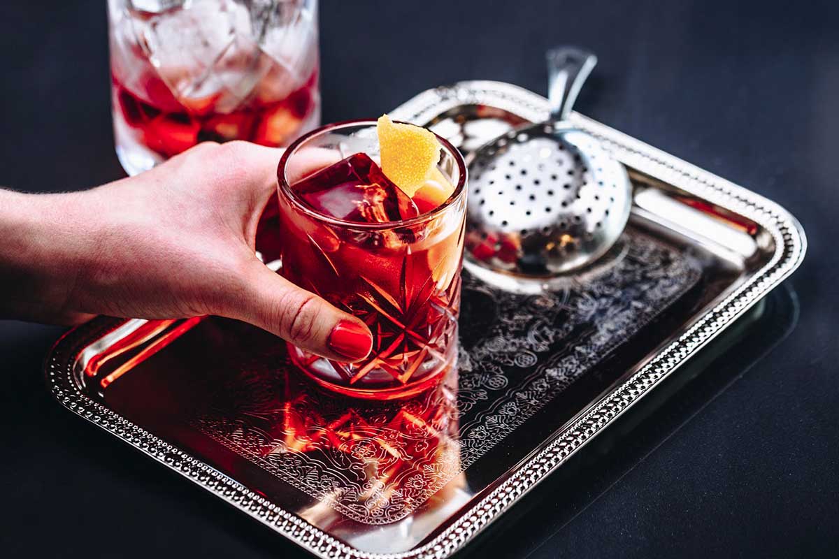 A Negroni in a rocks glass on a tray with a strainer and a mixing glass in the background. Negronis usually are made of equal parts