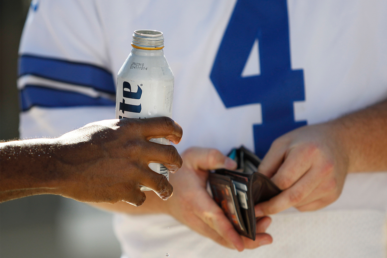 A concessions worker holding a beer out to an NFL football fan who is holding their wallet open. We look at the priciest beer in the NFL.