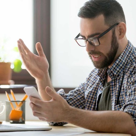 A man annoyed at a desk looking at his phone. The FCC seems poised to cut down on spam texting.