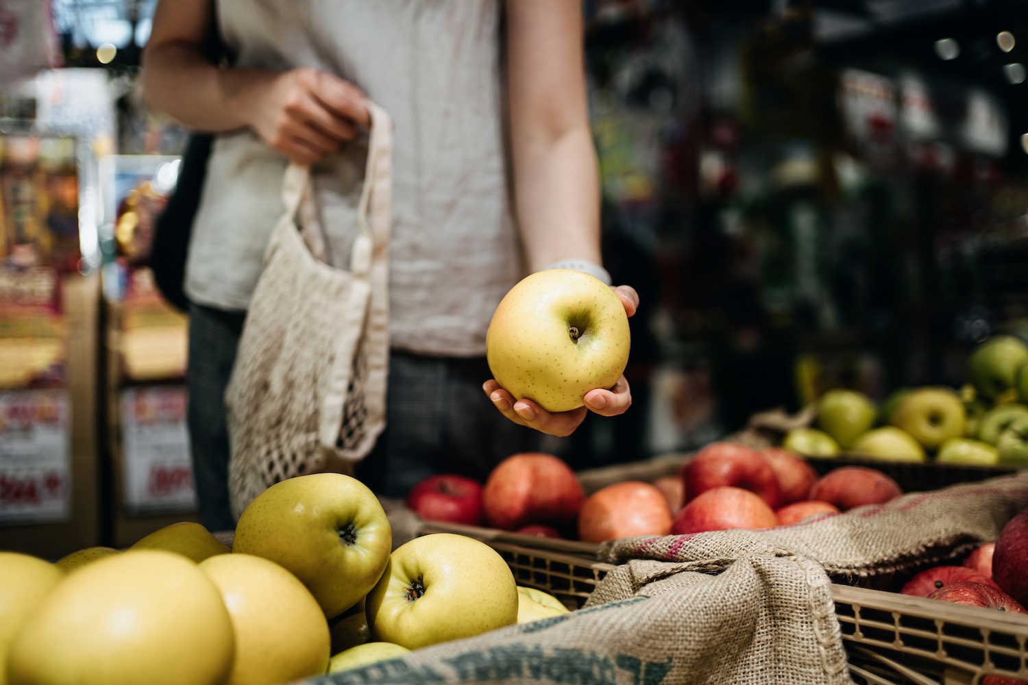 woman grocery shopping and holding a yellow apple