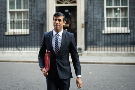 Rishi Sunak in a sharp black suit walking away from a goverment building