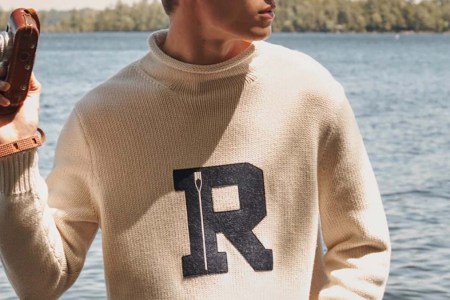 a model holding a camerain a cream cotton rollneck varsity sweater from J.Crew against a lake background