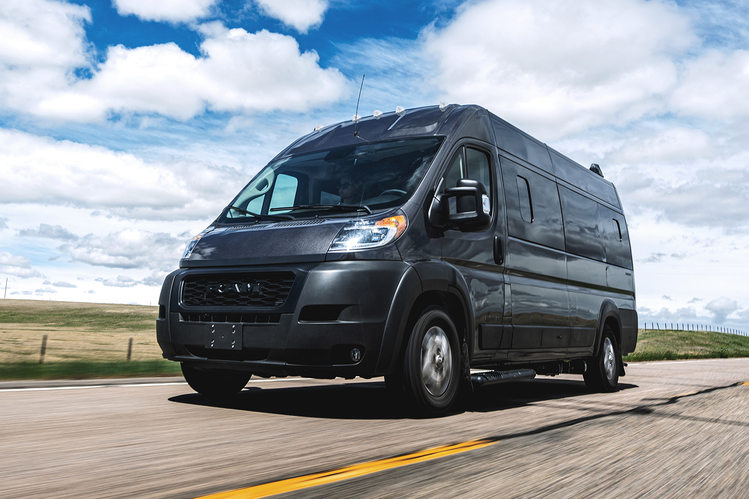 An Airstream Rangeline, a Class B motorhome built on a Ram ProMaster chassis, driving down the road under a blue sky with white clouds