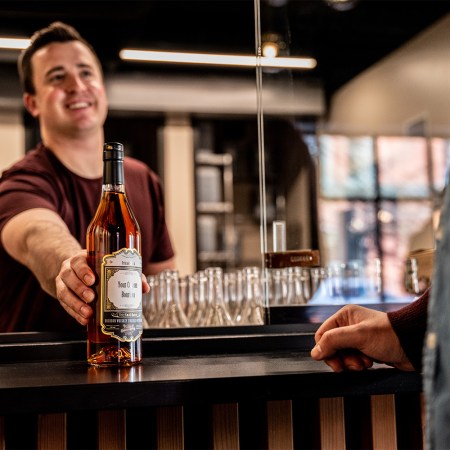 An employee at Barrels and Billets hands over a bottle of custom bourbon to a customer