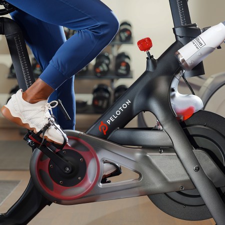 A person riding a Peloton Bike in a Hilton hotel with a branded water bottle in the holder