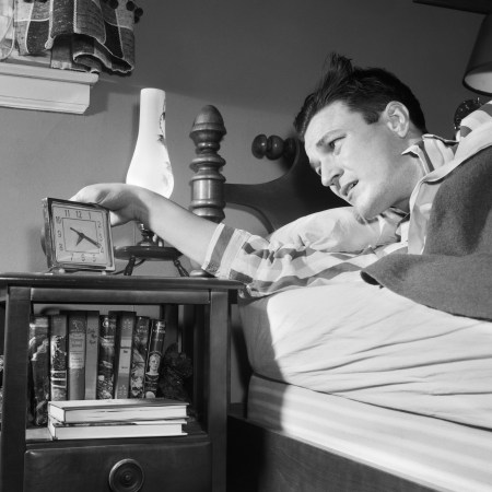 A black and white photo of a 1950s man checking his alarm clock.