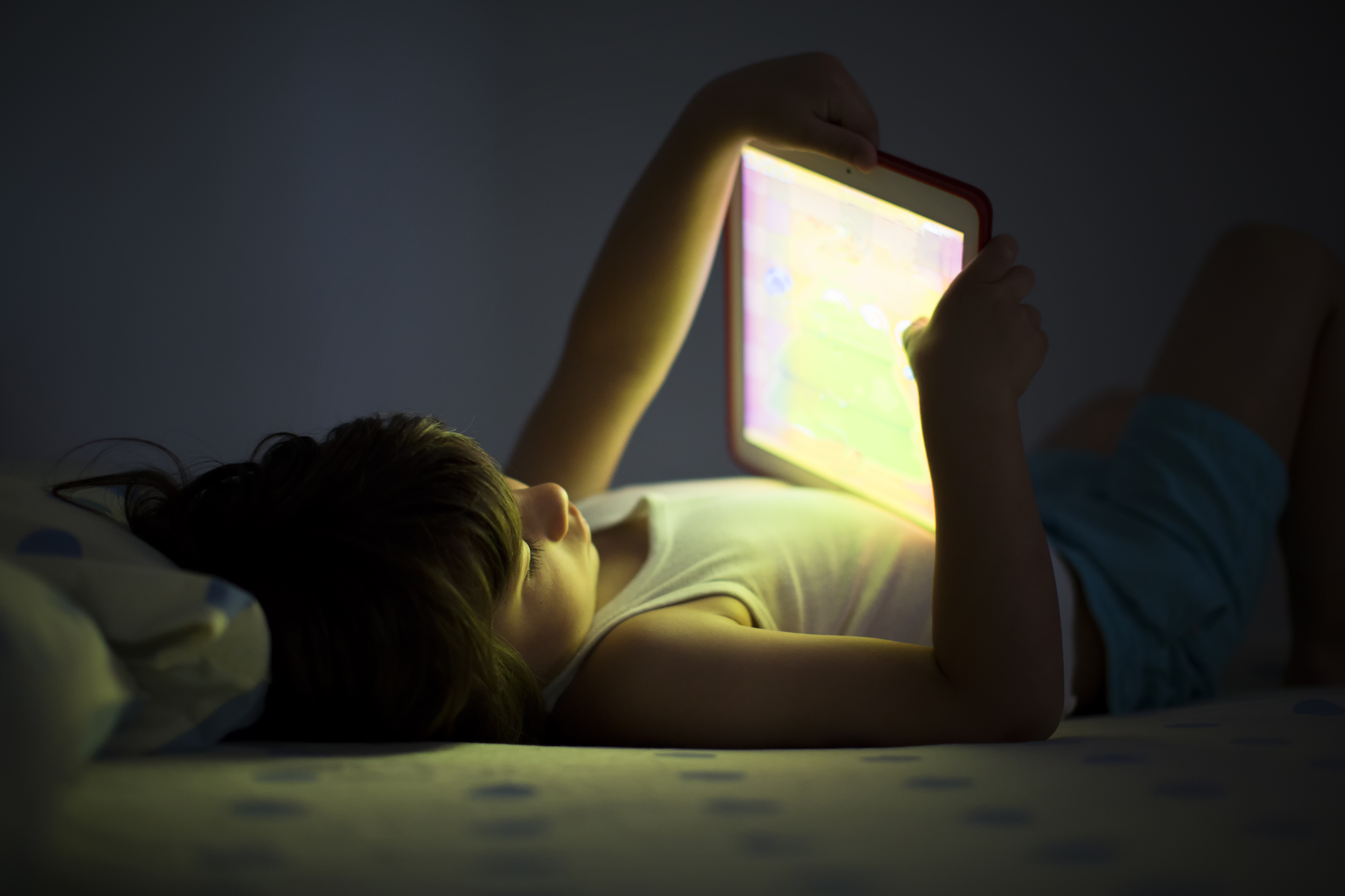 A young child holding an iPad in a dark bedroom.