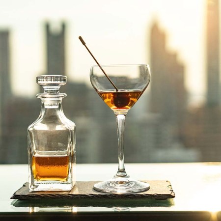 Photo of alcohol in a decanter and a cocktail in a coupe glass overlooking a skyline