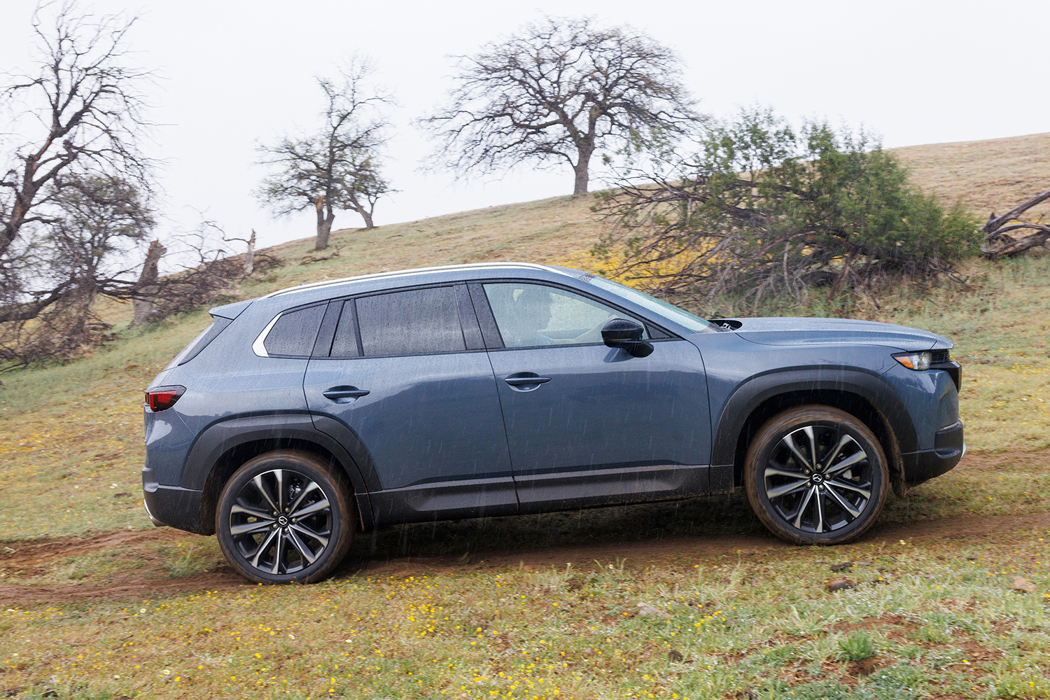 A blue Mazda CX-50 driving on a dirt road through the rain