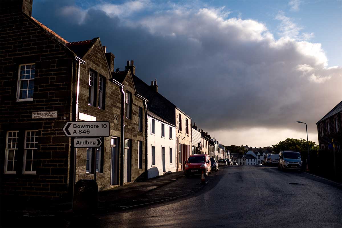 Looking down main street of Port Ellen sunlight with big storm clouds - stock photo. Peat supplies from Port Ellen may be curtailed in the next two years.