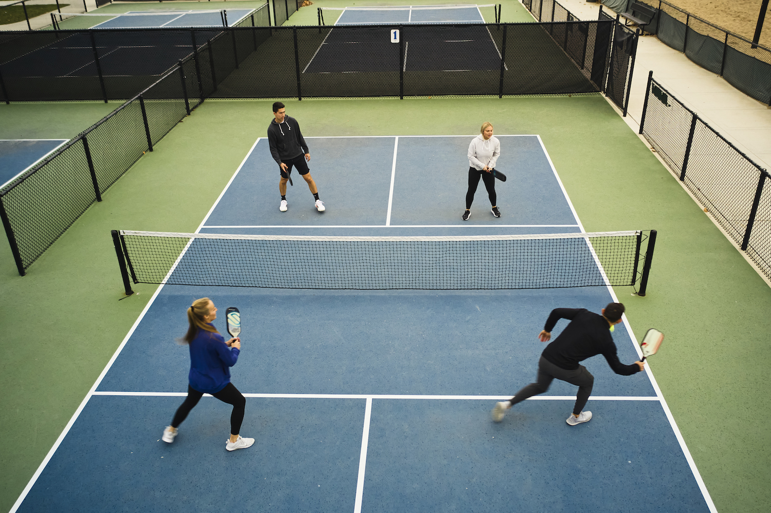 A group of young adults playing Pickleball on an outdoor court