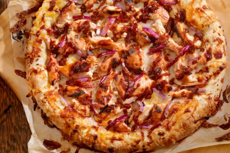 bbq chicken pizza with red onions on parchment paper