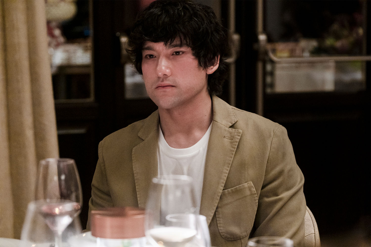 a character in a blazer and tee-shirt at in a dinner table from the White Lotus