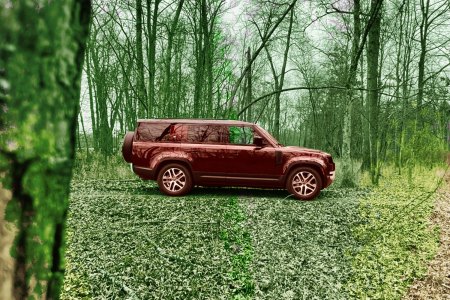 A maroon Land Rover in the woods in fall with lots of leaves