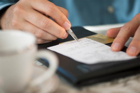 Close-up of a man signing a bill at a restaurant. Service charges at restaurants are increasing, but customers don't really know where the money is going