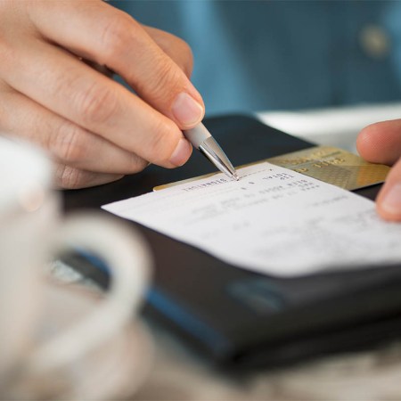 Close-up of a man signing a bill at a restaurant. Service charges at restaurants are increasing, but customers don't really know where the money is going