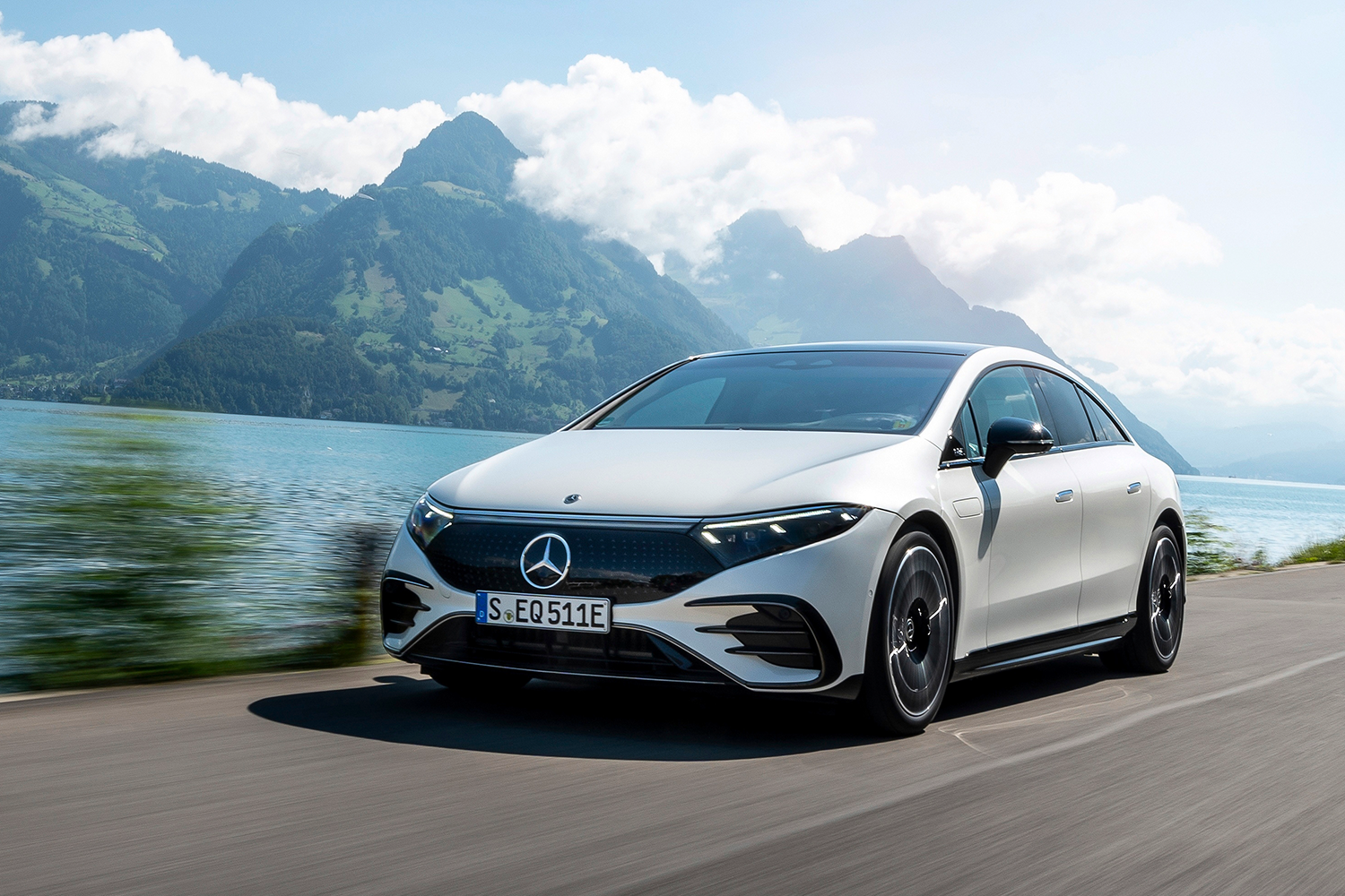 A white Mercedes-Benz EQS 580 4MATIC driving during the day with mountains in the background