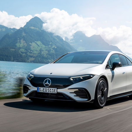 A white Mercedes-Benz EQS 580 4MATIC driving during the day with mountains in the background