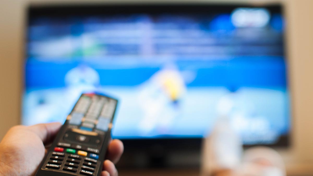 A person holding a TV remote and looking at a blurry screen while holding a TV remote. There are several settings you should change on your TV as soon as you get a new one.