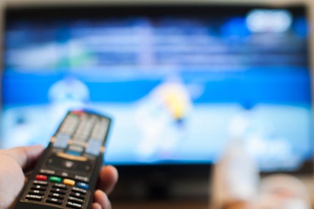 A person holding a TV remote and looking at a blurry screen while holding a TV remote. There are several settings you should change on your TV as soon as you get a new one.