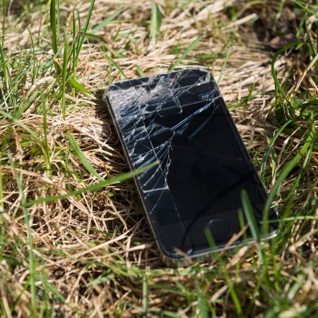 A shattered smartphone lying in a patch of grass.