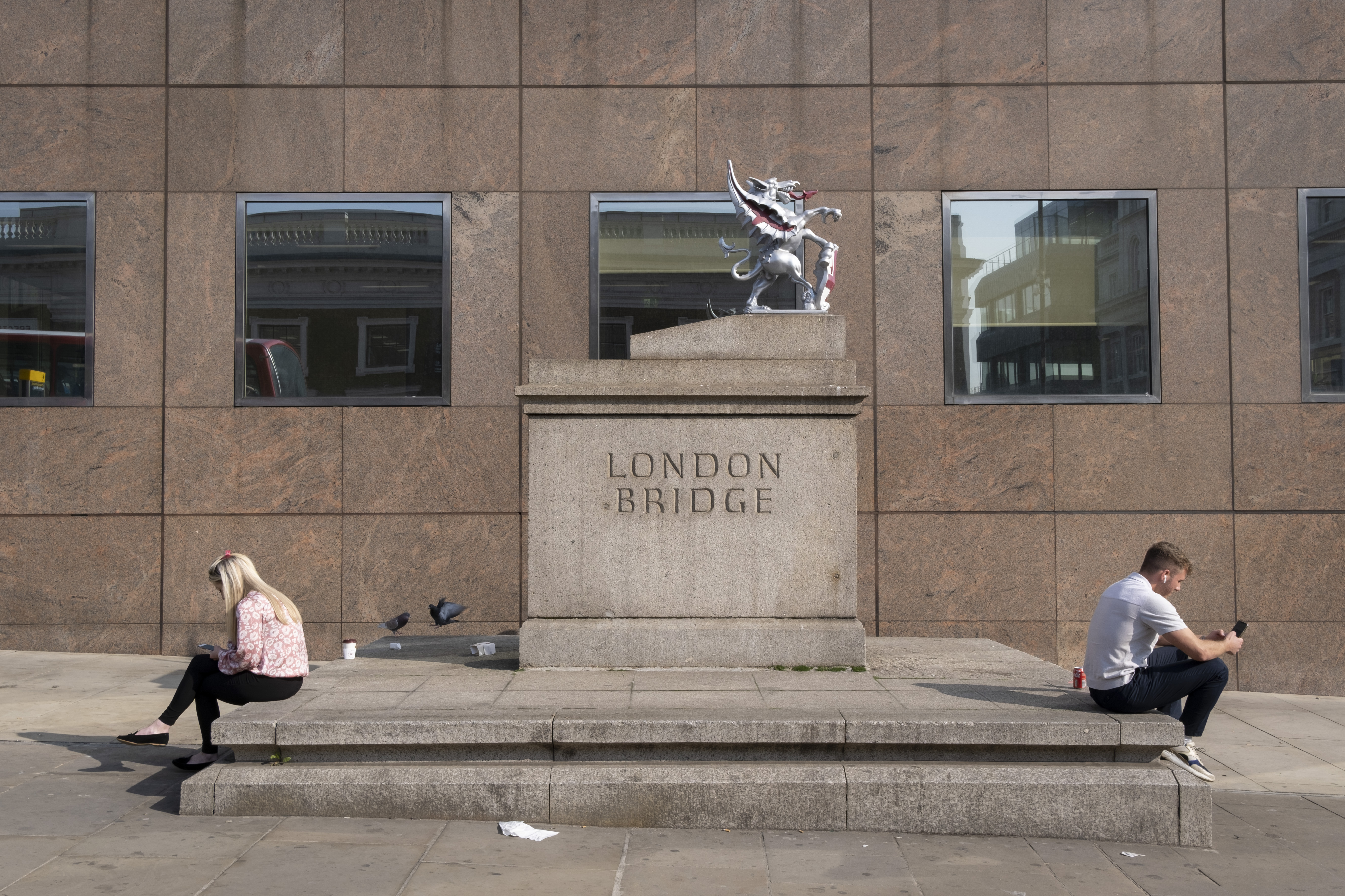 A man and woman sit on their phones back to back on either side of a statue.