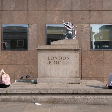 A man and woman sit on their phones back to back on either side of a statue.