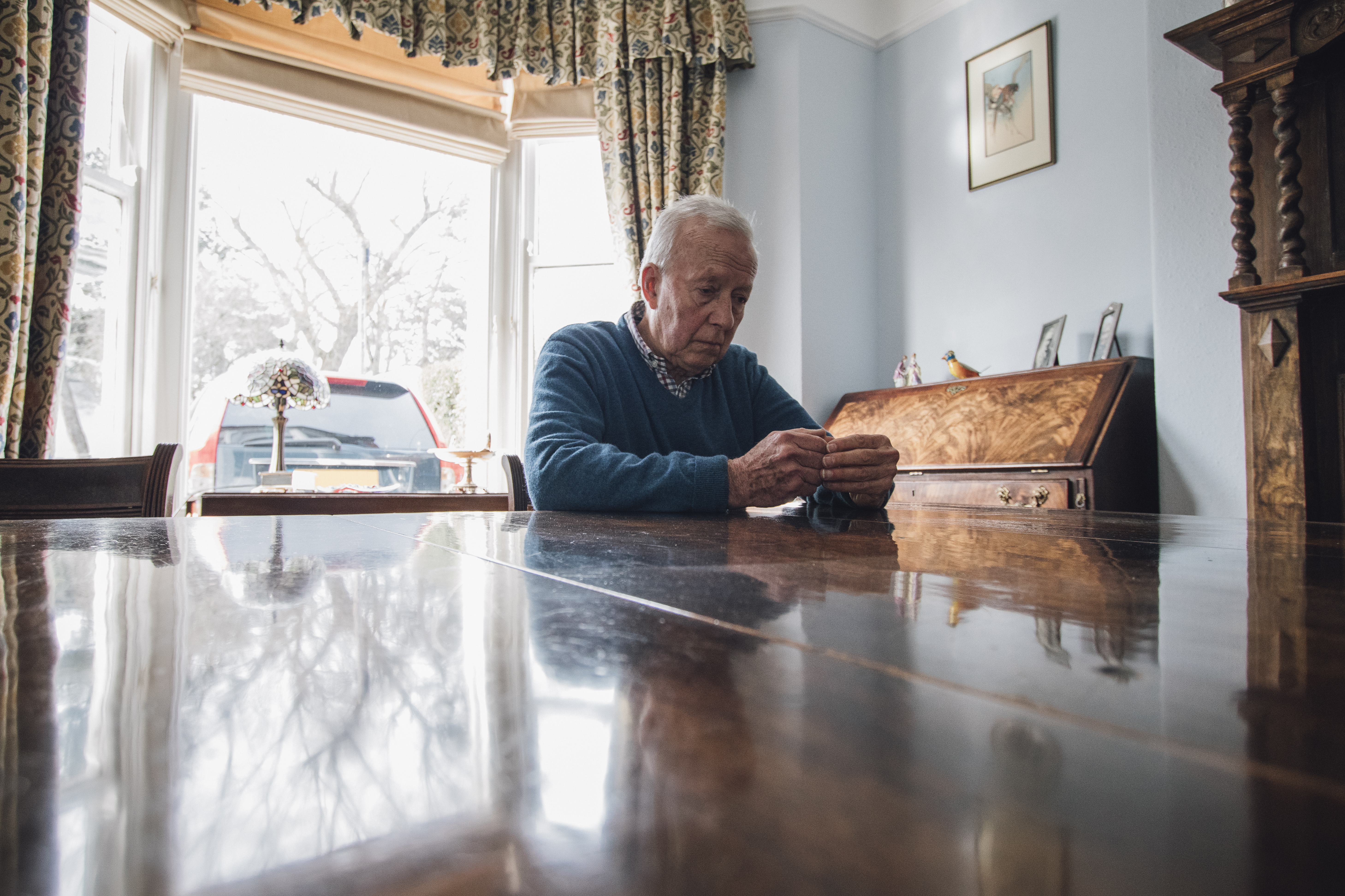 An old man sits alone at his living room table.