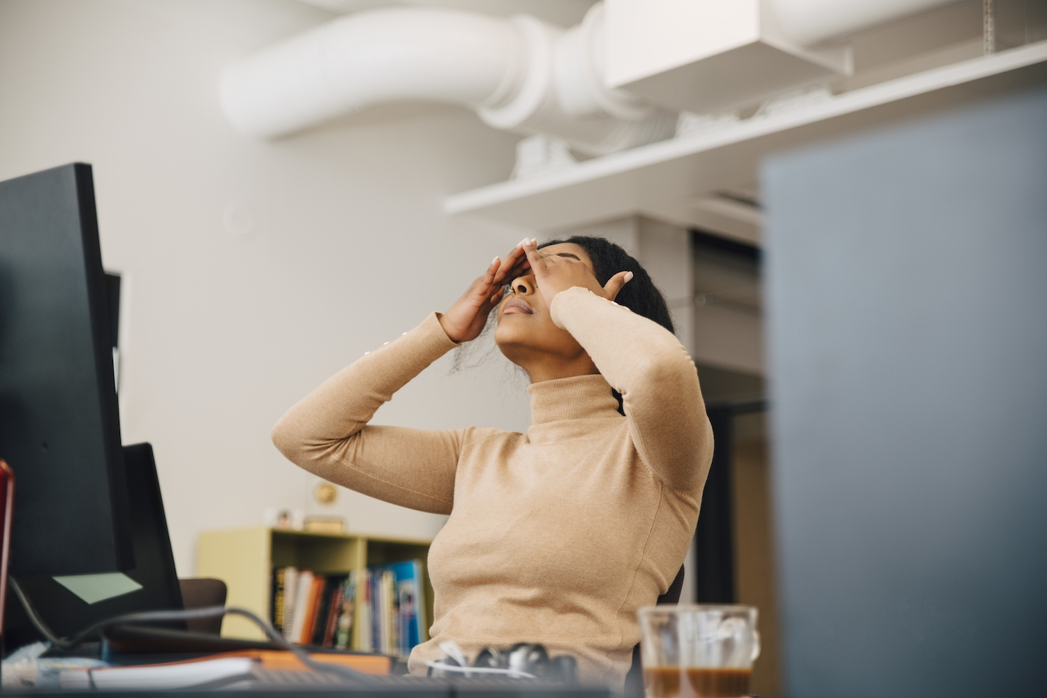 Frustrated female worker rubbing her eyes in front of a computer sitting in creative office