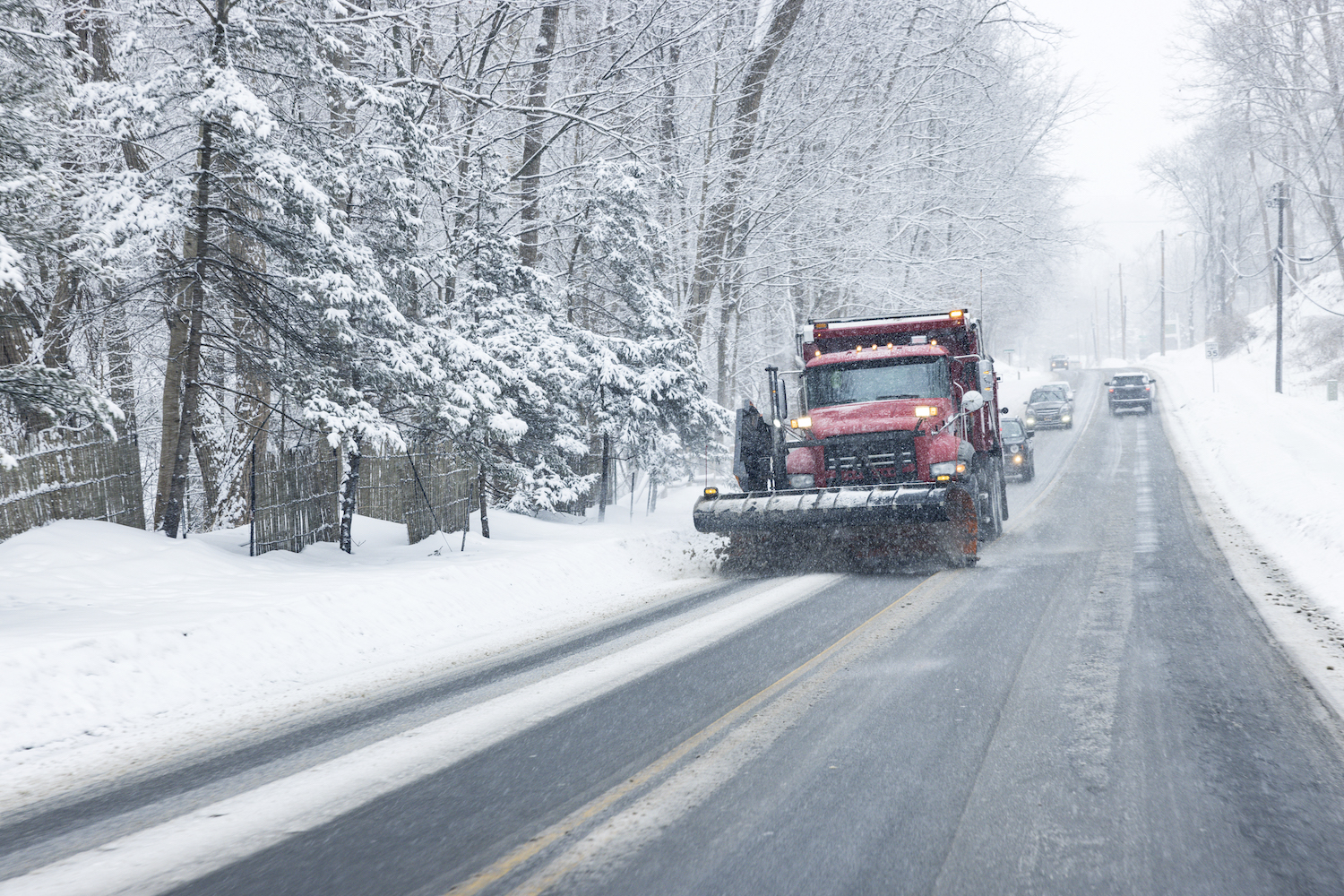 A red snowplow plowing snow up a hill on a steep rural road