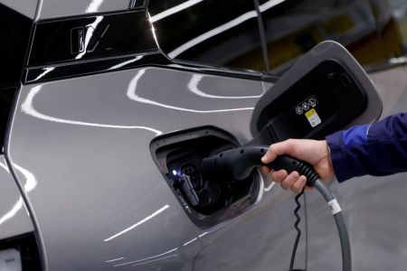 A hand holding an EV charger into the charging port of an electric car