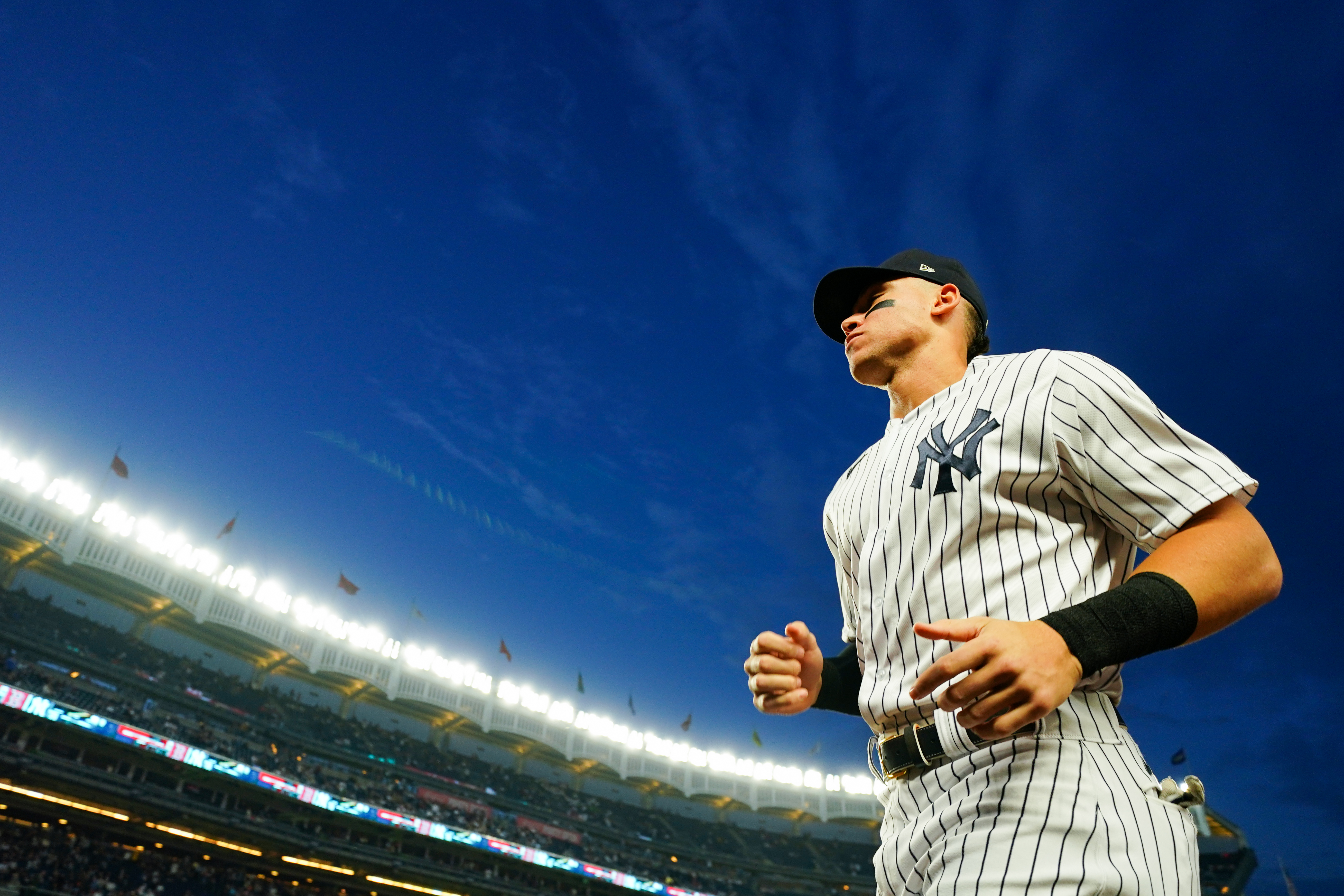 Aaron Judge running towards the dugout during a night game at Yankee Stadium.