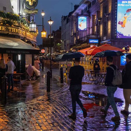 On a rainy night in Soho, Londoners walk across a pedestrianised Old Compton Street. Due to increased public urination, a splashback paint is being applied to various areas around the city.