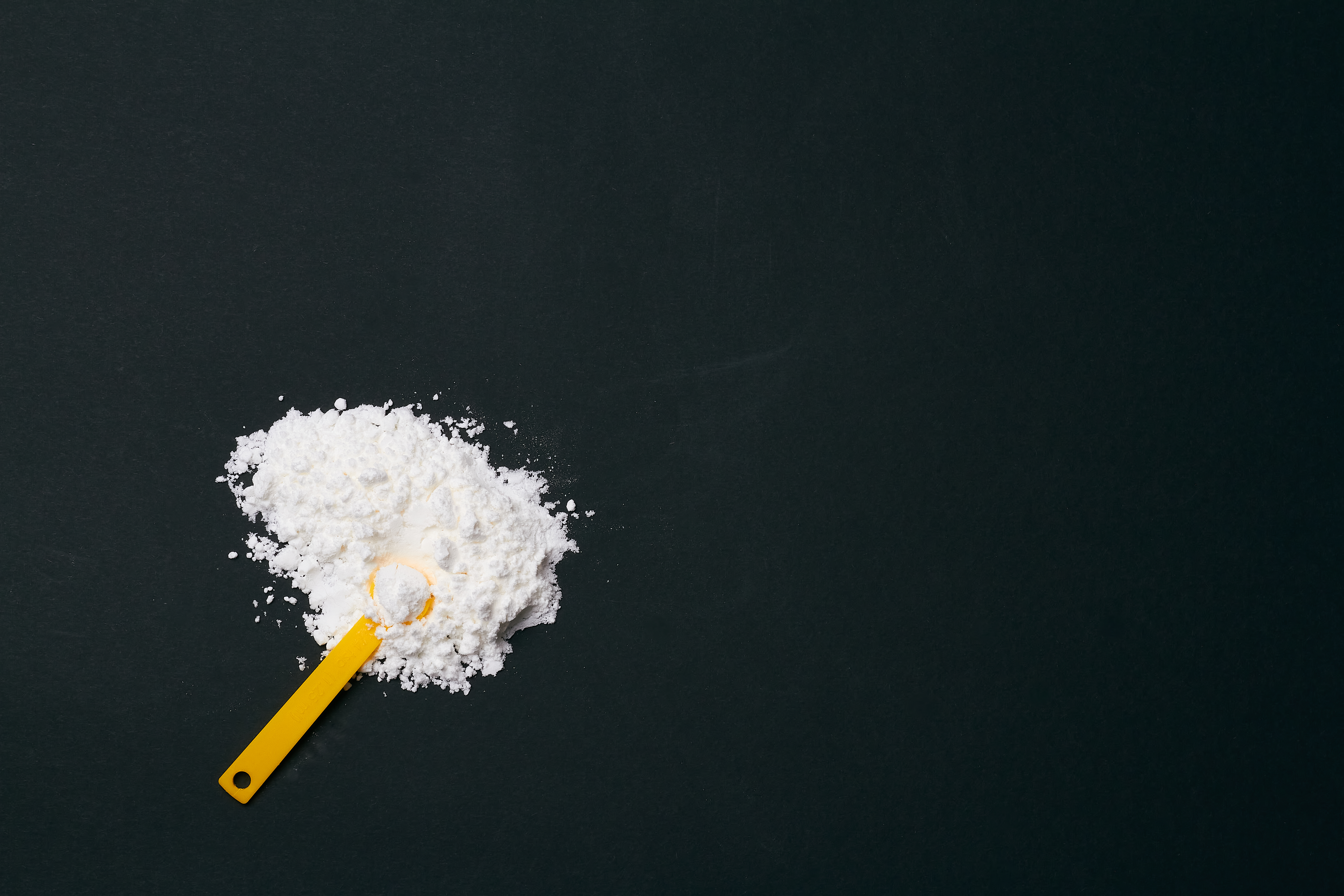 A photo of creatine powder on a black background, with a scoop.