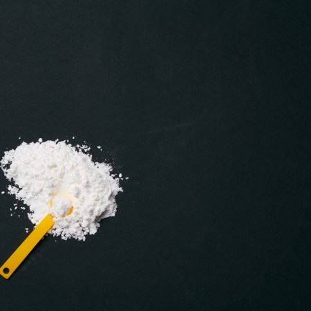 A photo of creatine powder on a black background, with a scoop.