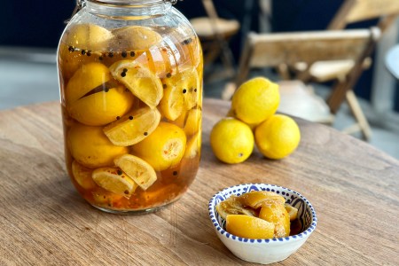 a jar and bowl of preserved lemons sitting on a wooden table