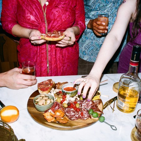 people standing around a table with cocktails eating from a charcuterie platter