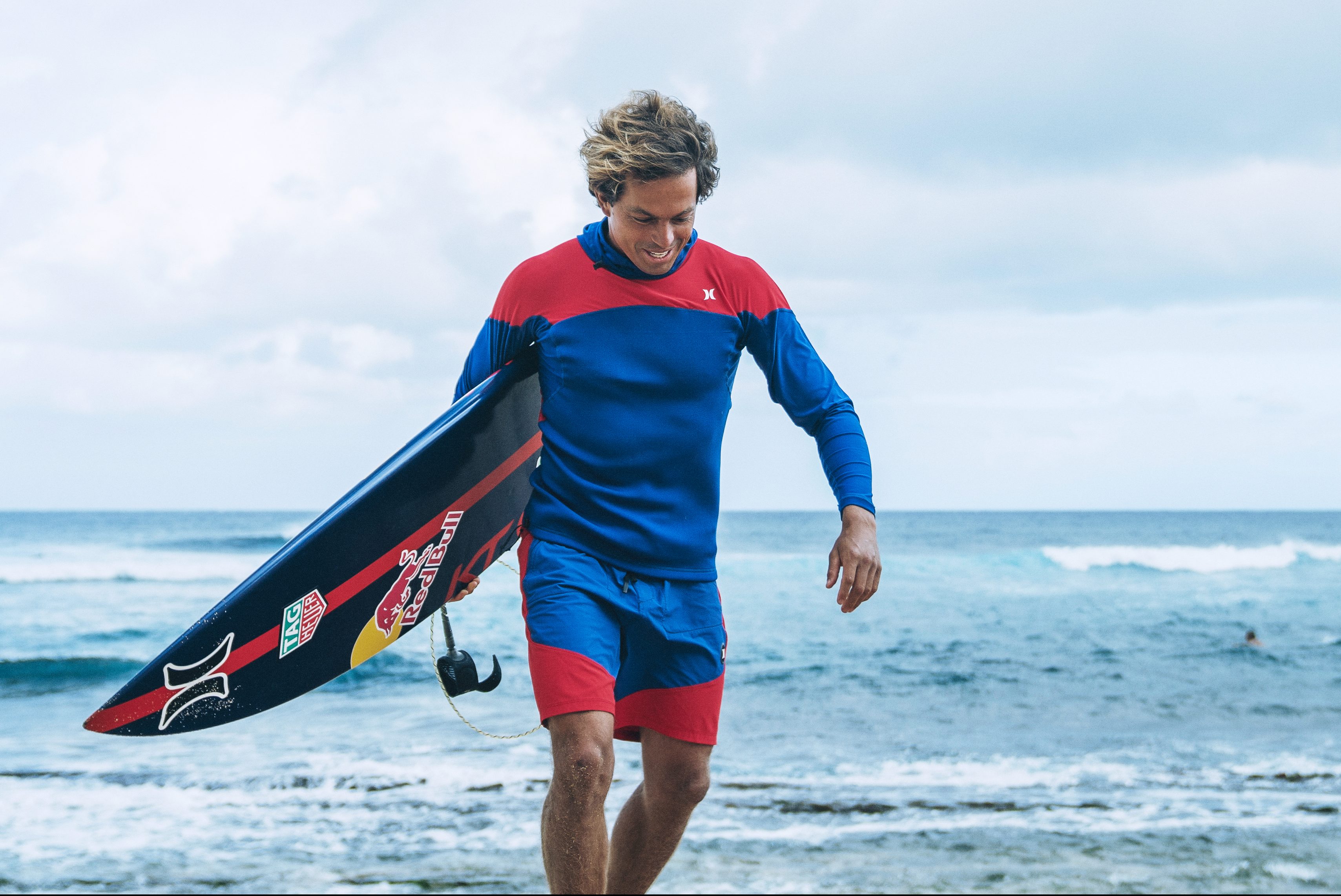 Kai Lenny holding his surfboard.