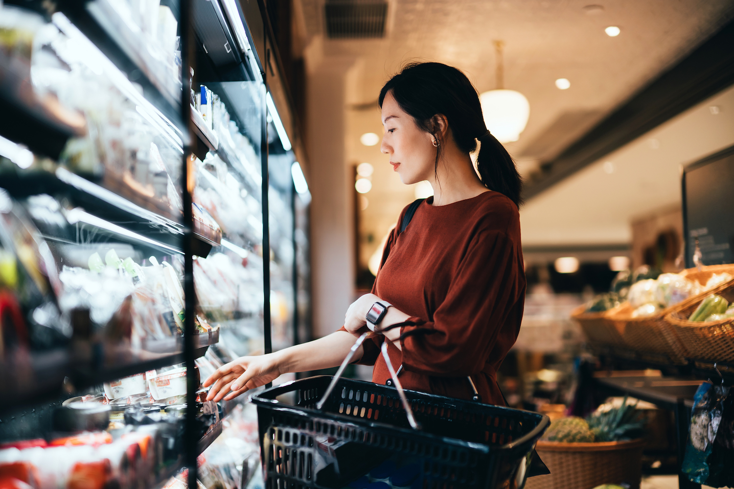 woman in a red shirt carrying a shopping basket while grocery shopping