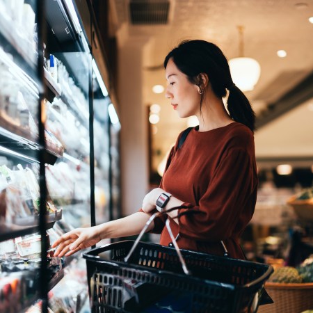 woman in a red shirt carrying a shopping basket while grocery shopping