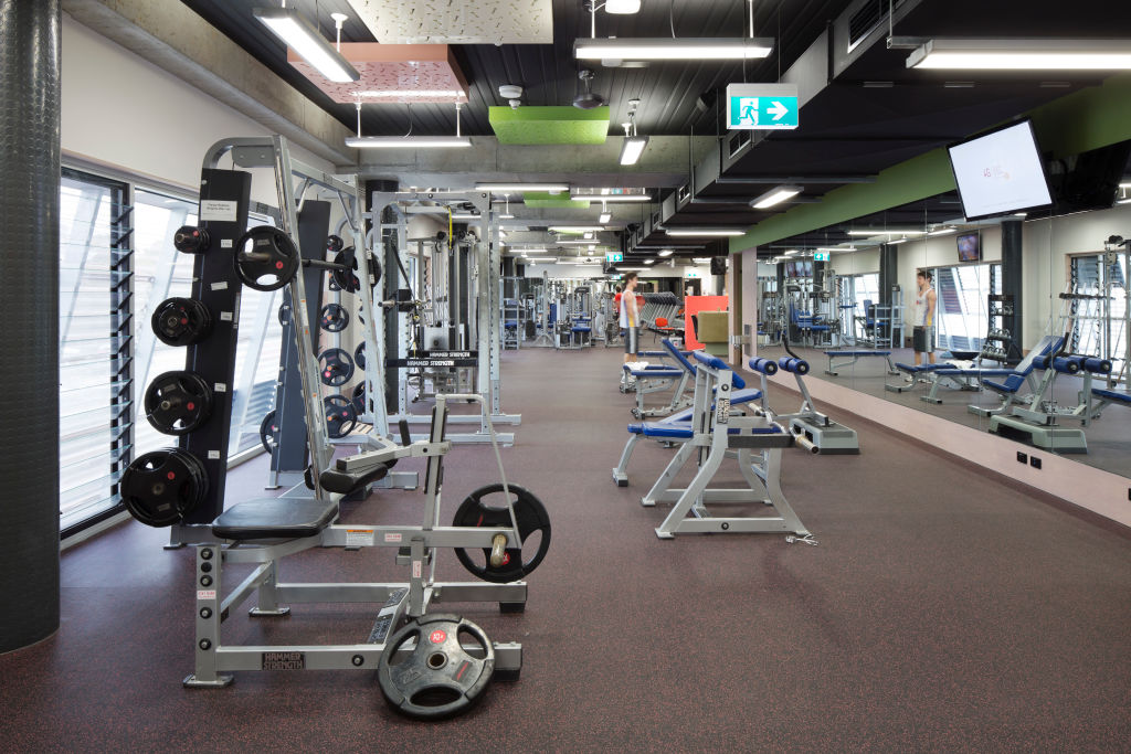 A man looking into a gym mirror while working out among fitness equipment. Are the many mirrors in gyms actually bad for exercising?