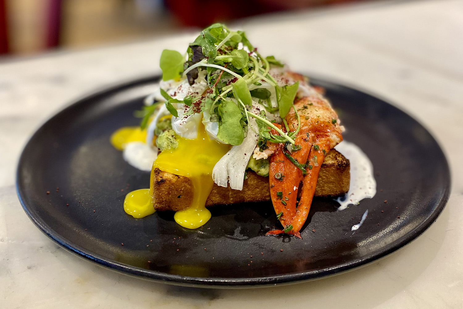 lobster toast with runny eggs on a black plate