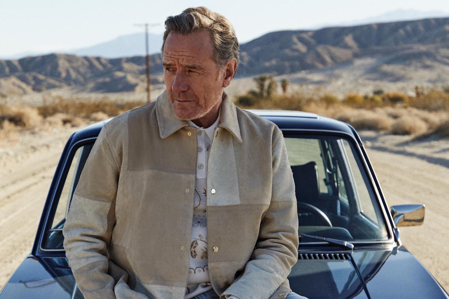 a photo of Bryan Cranston in Kith clothing siitting on a vintage car in the desert