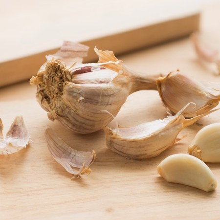 a head of garlic next to two unpeeled cloves and two peeled cloves