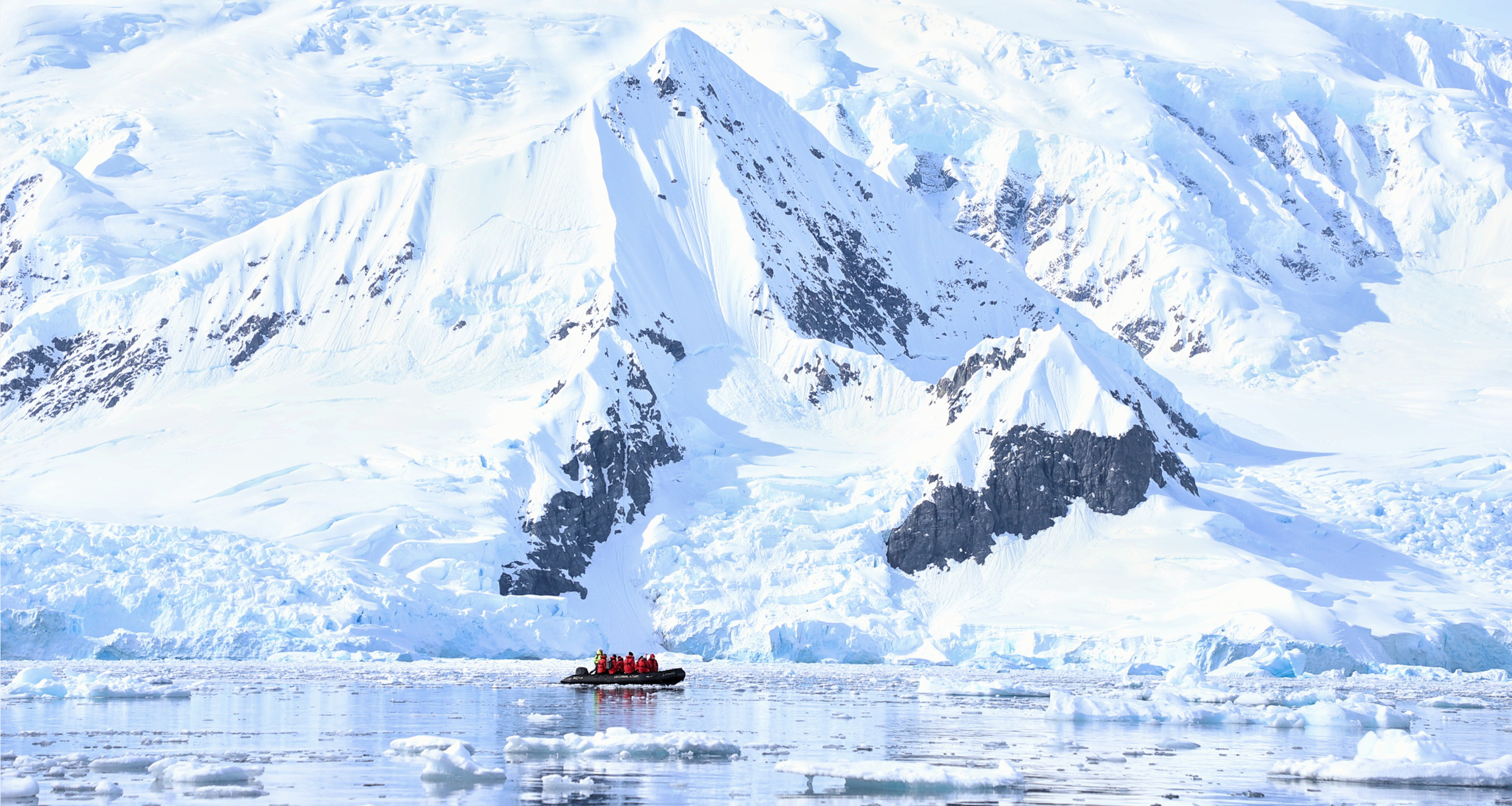 A Zodiac boat from travel company Abercrombie & Kent ferrying travelers past mountains and icebergs during an Antarctica cruise