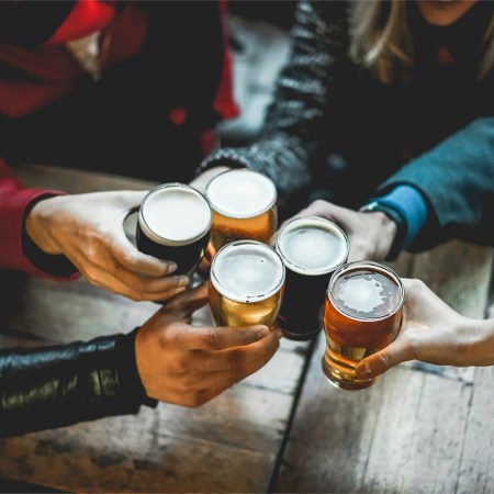 Young group of people having fun cheering with beer outdoor at bar restaurant - Soft focus on right hand holding glass