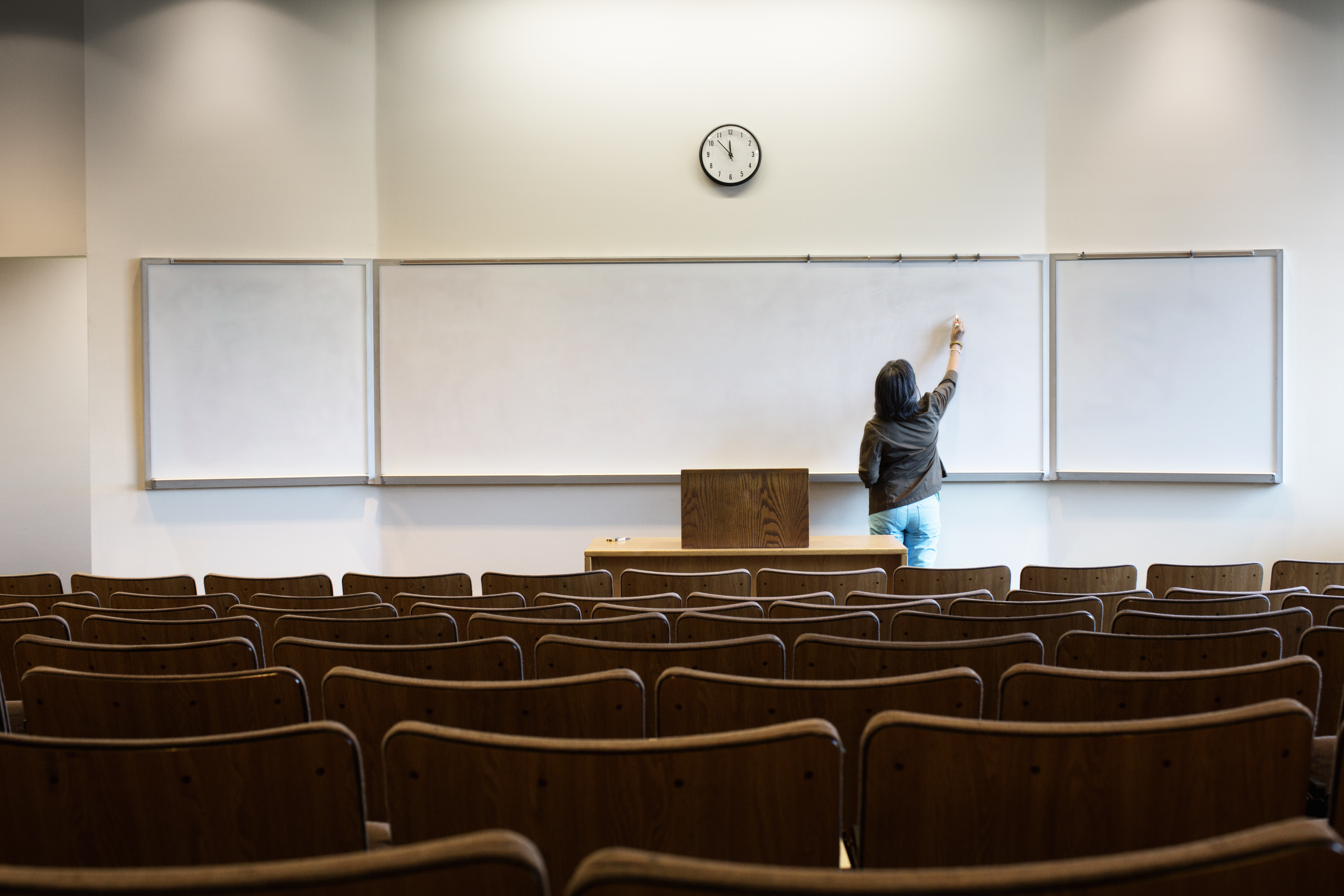 A woman writing on a whiteboard in a lecture hall.